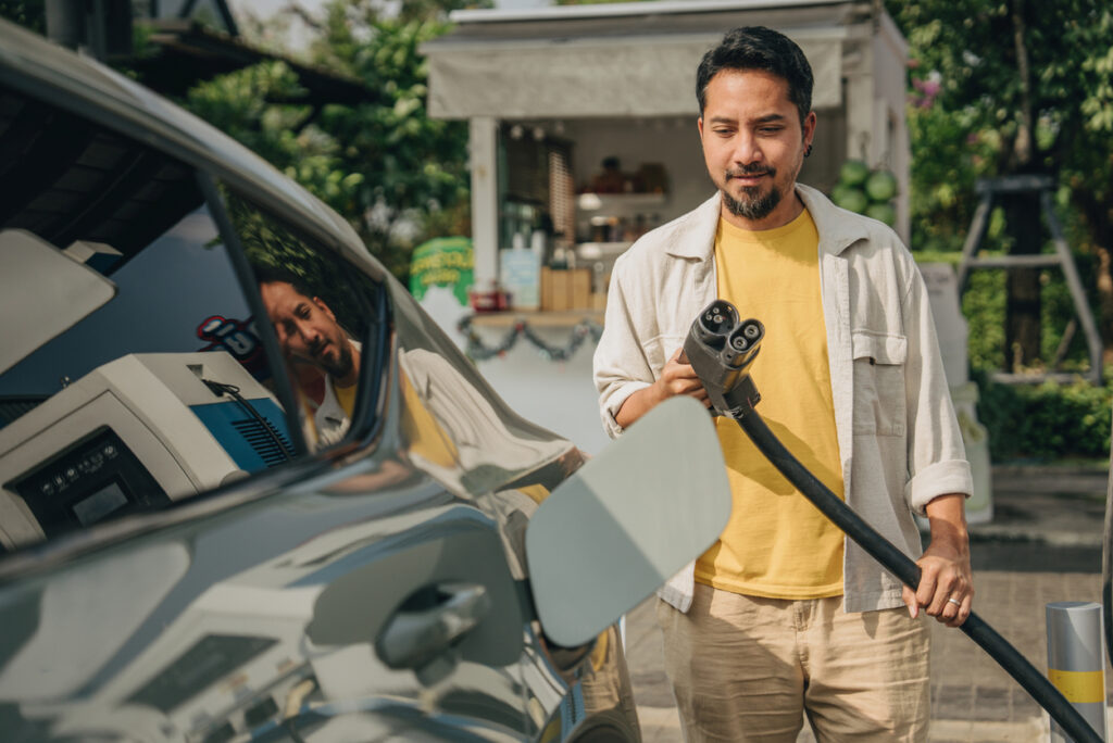 Asian man is opening the car hood to refuel his electric car at Bangkok, Thailand